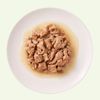 Ein weißer Teller, gefüllt mit feuchtem, zerriebenem Dosenfutter für Katzen in einer leichten Brühe, der eine weiche, fleischige Textur zeigt.