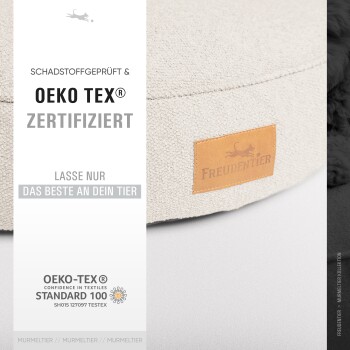 Ein beiges Haustierbett mit einem Lederetikett mit der Aufschrift "Freudentier", mit Text über Oeko-Tex-Zertifizierung und Sicherheitsstandards.