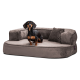 Ein schwarz-brauner Dackel, der bequem auf einem plüschigen, grauen Hundebett mit erhöhten Seiten und einem kleinen Kissen liegt.