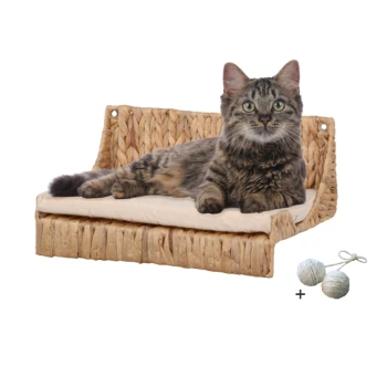 Eine entspannte getigerte Katze liegt auf einem geflochtenen Katzenbett mit einem beigen Kissen, begleitet von zwei kleinen Spielbällen.