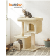 Ein gemütlicher beiger Kratzbaum mit zwei Ebenen; eine graue getigerte Katze sitzt oben, während eine weiße Katze mit grauen Flecken aus einem unteren Fach herauskommt.