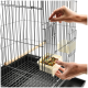 Eine Person, die einen Futternapf mit buntem Vogelfutter in einen Drahtvogelkäfig stellt, mit einer sichtbaren Holzstange im Inneren.