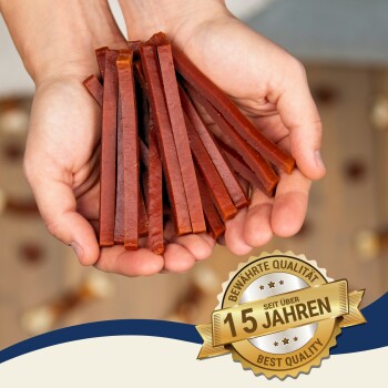 Hände halten einen Stapel von Hundeleckerlis mit einem Abzeichen, das "Beste Qualität" und "15 Jahre" auf Deutsch angibt.