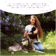 Eine Frau hält eine schwarze Katze neben einem wolfähnlichen Hund in einem Garten. Text: "Als Tierheilerin liebe ich Wolfsbacher Natur." - Lena Huber.