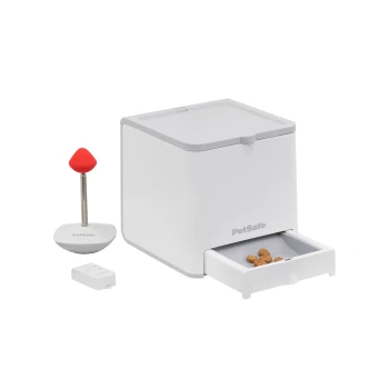 PetSafe Futterspender mit einem weißen Behälter, einem roten Ausgabestab und einer kleinen Schublade, die Hundeleckerlis zeigt.