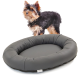 Ein kleiner schwarz-brauner Yorkshire Terrier steht neben einem runden, grauen Hundebett mit gepolstertem Rand, das ein schlankes Design zeigt.