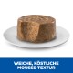 Ein rundes Stück Haustierfutter mit einer mousseartigen Textur, teilweise abgebissen, auf einem weißen Teller präsentiert. Der Text lautet "WEICHE, KÖSTLICHE MOUSSE-TEXTUR."