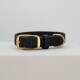 Schwarzes Leder-Haustierhalsband mit einer goldenen Schnalle und Schlaufe, auf einem hellgrauen Hintergrund präsentiert.