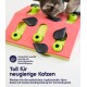 Eine graue Katze spielt mit einem bunten Puzzle-Spielzeug auf einer pinken Basis, das grüne und schwarze Elemente enthält. Der Text spricht über mentale und körperliche Beschäftigung.