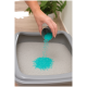 Hand gießt blaue geruchsneutralisierende Kristalle in eine graue Katzenstreu-Kiste, die mit weißem Streu gefüllt ist.