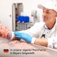 Ein Arbeiter in einem weißen Kittel und blauen Handschuhen hantiert mit rohem Fleisch in einer sauberen, industriellen Küche. Text: "In unserer eigenen Manufaktur in Bayern hergestellt."