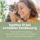 Grau getigerte Katze, die von einer Person mit lockigem Haar gehalten wird, deutscher Text über sanftes Öl für empfindliche Verdauung.