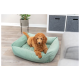 Ein flauschiger, goldbrauner Welpe, der in einem hellgrünen Hundebett entspannt, mit einer Topfpflanze und Aufbewahrungsboxen im Hintergrund.
