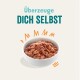 Bol de nourriture pour animaux avec un mélange texturé, entouré de graphiques orange ludiques, avec le texte "Überzeuge DICH SELBST."