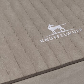 Eine Nahaufnahme eines beigen Haustierbettes mit vertikalen Nähten, das das gestickte Logo "KNUFFELWUFFF" und eine Silhouette eines Hundes zeigt.