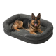 Deutscher Schäfer, mit heraushängender Zunge, liegt auf einem grauen Hundebett mit erhöhten Seiten auf weißem Hintergrund.