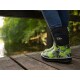 Grün-schwarz gemusterte Gummistiefel, die von einer Person auf einem Holzsteg an einem ruhigen, bewaldeten Wasserlauf getragen werden.