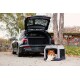 Ein schwarzer SUV mit offenem Kofferraum, der neben einer tragbaren Hundebox geparkt ist, in der ein flauschiger braun-weißer Hund ruht.