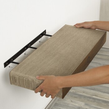 Eine Person installiert einen wandmontierten Katzekratzer, der eine strukturierte beige Oberfläche und eine Holzbasis aufweist, an einer schwarzen Metallhalterung.