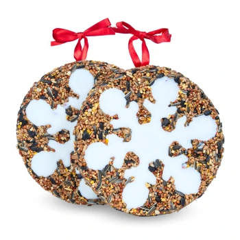 Zwei dekorative Vogelfutterornamente in Form von Schneeflocken, verziert mit weißem Zuckerguss und mit roten Bändern gebunden.