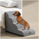 Kleiner brauner Dackel mit orangefarbener Bandana, der auf grauen Haustiertreppen neben einem Bett in einem modernen Raum steht.
