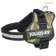 Ein hunde Geschirr mit Camouflage-Muster und schwarzem Riemen, ausgestattet mit einem Metall-D-Ring und einem großen Etikett, das "JULIUS-K9 IDC®POWER" liest.