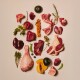 Assortiment de viandes crues et de produits sur fond pâle : pilon de poulet, côtelettes d'agneau, steaks, cœurs, foie, citrouille, herbes.