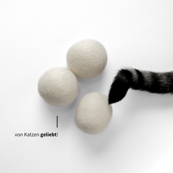 Drei weiße Filzkugeln auf einer weißen Oberfläche, mit dem gestreiften Schwanz einer Katze, die nach ihnen greift, und dem Text "von Katzen geliebt!" in der Nähe.