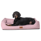 Ein schwarz-brauner Hund, der auf einem weichen rosa Haustierbett mit einem kleinen Kissen entspannt, mit einem Holzschild, das "tierlando" beschriftet ist.