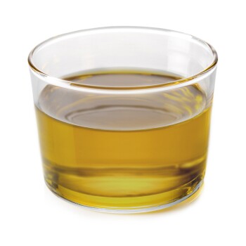 Ein klares Glas gefüllt mit einer goldgelben Flüssigkeit, die wie Öl aussieht, vor einem weißen Hintergrund.