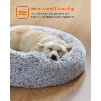 Graues rundes flauschiges Haustierbett mit zusammengerolltem cremefarbenem Hund auf Holzfußboden; sichtbarer Text 'Weich und flauschig' und deutscher Werbeslogan.