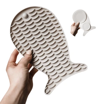 Eine Person hält eine große, beige Silikon-Haustierfütterungsmatte in Fischform, mit strukturierten Schuppen für besseren Halt.