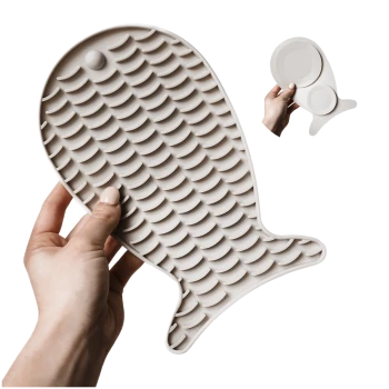 Eine Person hält eine große, beige Silikon-Haustierfütterungsmatte in Fischform, mit strukturierten Schuppen für besseren Halt.