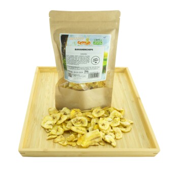 Getrocknete Bananenchips in einer Kraftpapiertüte mit der Aufschrift "Bananenchips," mit Frischegarantie und Nährwertinformationen, auf einem Holztablett präsentiert.