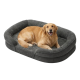 Golden Retriever lächelnd und liegend in einem grauen Plüsch-Ovalhundebett auf weißem Hintergrund