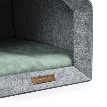 Graues Haustierbett mit einem weichen grünen Kissen innen, mit einem Lederschild, auf dem 'rexproduct.com' steht.