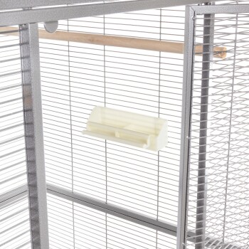 Innenansicht eines Haustierkäfigs mit einer Holzstange und einer weißen Fressschüssel, die an der Drahtwand montiert ist.