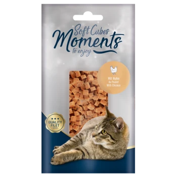Verpackung von Soft Cubes Moments Haustierleckerlis mit einer getigerten Katze, die neben einem transparenten Fenster liegt, das weiche, gewürfelte Hühnergeschmack-Cubes zeigt.