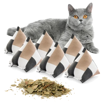 Eine graue Katze mit leuchtend orangefarbenen Augen liegt neben sechs dreieckigen Katzenminzkissen in beige, weiß und schwarz, mit getrockneter Katzenminze, die davor verstreut ist.