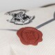 Close-up of a white fabric with a red wax seal embossed with an "H" and a black Hogwarts crest in the background.
