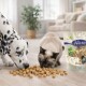 Dalmatiner und Siamkatze fressen kleine Snackwürfel auf dem Boden, Lyra Pet-Tüte mit der Aufschrift 'Nature Power' sichtbar.