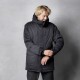 Eine Person in einer schwarzen, isolierten Jacke mit Kapuze und Reißverschlusstaschen steht vor einem grauen Hintergrund.
