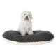 Ein kleiner, flauschiger weißer Hund sitzt glücklich auf einem plüschigen, ovalen Hundebett mit einem dunkelgrauen Oberteil und einem cremefarbenen Boden.