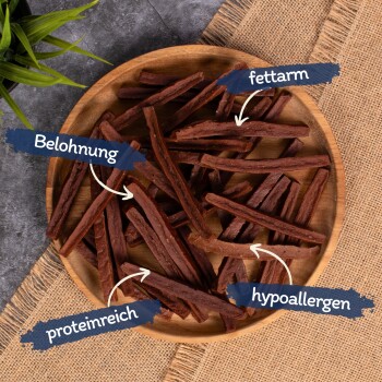 Ein Holzbrett mit langen Hundeleckerlis, beschriftet auf Deutsch: "Belohnung", "fettarm", "proteinreich" und "hypoallergen."