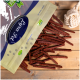 Eine Tüte mit Haustierleckereien mit der Aufschrift "Paw Treats", die lange, dünne, braune Stäbchen auf einer Holzoberfläche auskippt, mit einem Seilspielzeug in der Nähe.