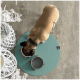Ein tanfarbener Hund mit einem schwarzen Halsband frisst aus einer weißen Schüssel, die mit Kibble gefüllt ist, auf einem runden türkisfarbenen Platz. Eine zweite Schüssel für Wasser steht in der Nähe.