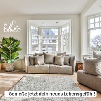 Helles Wohnzimmer mit einem gemütlichen grauen Sofa, Kissen, einer Topfpflanze und großen Fenstern. Text: "Genieße jetzt dein neues Lebensgefühl!"