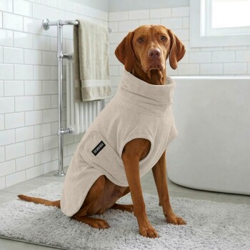 Ein beiger Hundemantel mit weicher Textur, der eine Seitentasche und ein Etikett mit der Aufschrift 'THE DOG IDEA' hat.