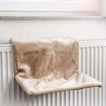 Ein weiches, beiges Haustierregal, das auf einem weißen Heizkörper ruht, entworfen für Katzen, um bequem am Fenster zu entspannen.