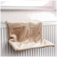 Ein weiches, beiges Haustierregal, das auf einem weißen Heizkörper ruht, entworfen für Katzen, um bequem am Fenster zu entspannen.